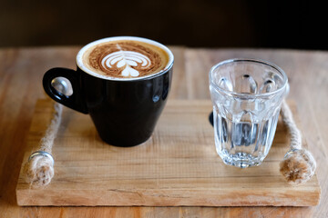 cappuccino coffee cups and warm water were served together on a wooden tray.