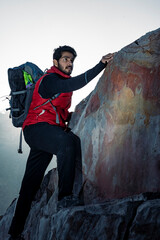 young indian climber and traveler climbing up the mountain rock during sunset. Adventure and sports concept.