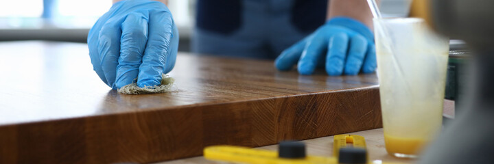 A carpenter in a workshop polishes a wooden surface. Man in gloves varnishes a board