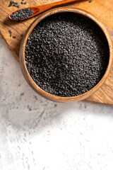 Black sesame seeds in a wooden bowl on a gray background close-up. Copy space for text.