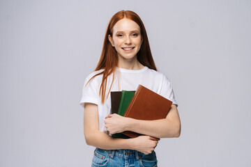 Smiling happy young woman college student wearing T-shirt and denim pants holding book on isolated...