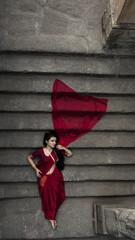 Portrait of beautiful Indian girl in heritage stepwell wearing traditional Indian red saree, gold...