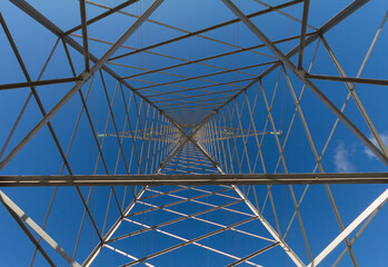 Low shot within a power transmission tower on a blue sky. Perfect symmetry.