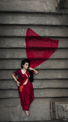 Portrait of beautiful Indian girl in heritage stepwell wearing traditional Indian red saree, gold...