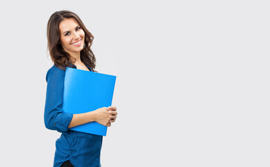 Portrait of happy smiling brunette businesswoman with blue folder, with blank copy space area for slogan or text, posing at studio against grey background