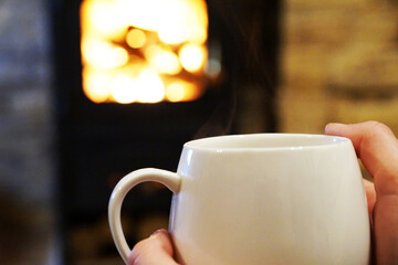 female hands hold a cup of hot tea on the background of a burning fireplace