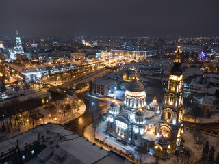 Holy Annunciation Cathedral illuminated in winter snowy night lights. Aerial view Kharkiv city orthodox church on riverbank, Ukraine. Side view from air.