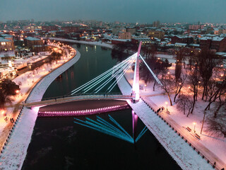 Bridge (Mist Zakokhanykh) across river in illuminated Skver Strilka in Kharkiv city center. Winter aerial evening colorful color graded photo