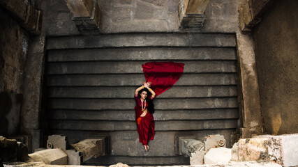 Portrait of beautiful Indian girl in heritage stepwell wearing traditional Indian red saree, gold...