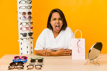 Young hispanic woman trying on glasses isolated screaming very angry and aggressive.