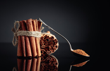 Ground cinnamon, cinnamon sticks, tied with jute rope on a black reflective background.