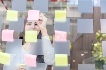 Professional women use post-it notes in a glass wall to write business plans and strategies to develop and grow to success.