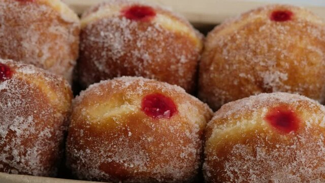 Close-up camera movement. Berliners. Donuts with raspberry jam lie on a serving tray on a white plate, a donut with a flowing filling. Delicious sweet donuts. Making donuts with jam.