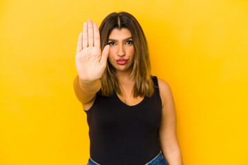 Young indian woman isolated on yellow background standing with outstretched hand showing stop sign,...