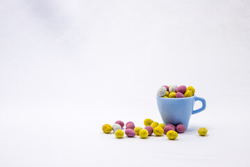 Chocolate Easter eggs on a white background. Small blue cup filled with chocolate eggs