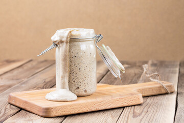 Natural fermented rye sourdough dripping down the jar stands on the cutting board. Healthy food