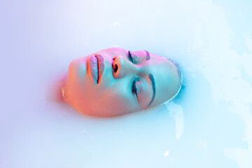 Calm beauty. Close up female face in the milk bath with soft white glowing in neon light. Copyspace for advertising. Modern neoned colors, foam. Beauty, fashion, style, bodycare concept. Attractive.