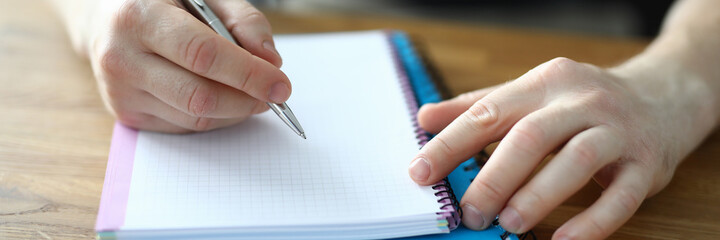 Male hands make notes in a notebook close up. Student guy holds a pen over a diary