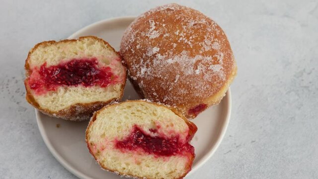 Berliners. Female hands put a donut with raspberry jam on a plate on a white background, a cutaway donut with a filling filling. Delicious sweet donut. Making donuts with jam.