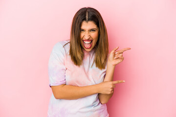 Young indian woman isolated on pink background pointing with forefingers to a copy space, expressing excitement and desire.