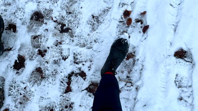 Pov top down of person with walking boots hiking on snowy path with many shoeprint of other hiker. Beautfiul bright winter day in nature. Slow motion track shot.