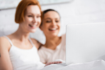 selective focus of laptop near cheerful interracial lesbian couple watching movie in bed