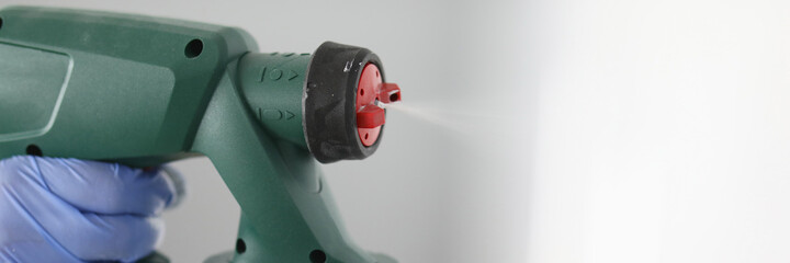 A hand in a glove holds special equipment for spraying paint close-up. Repairing the building from...