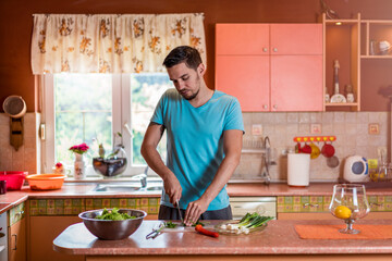 Fototapeta na wymiar Man in kitchen. Handsome young man with knife in kitchen preparing and cooking vegetarian meal