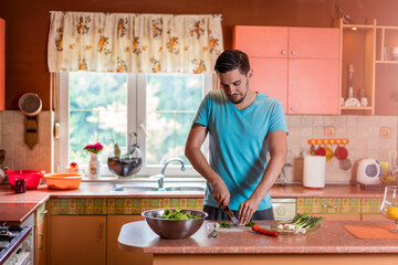 Obraz na płótnie Canvas Man in kitchen. Handsome young man with knife in kitchen preparing and cooking vegetarian meal