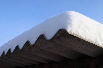 Fresh snow covered the roof with a thick layer against the blue sky, winter background