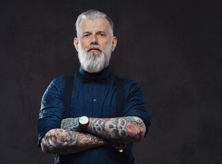 Handsome hipster grandfather with tattooed hands poses in dark background looking at camera.