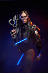 Obraz premium Atmospheric portrait of a female soldier with nude legs and eyewear posing in dark background with blue lights. Cyber woman with implant on her shoulder looking at camera.