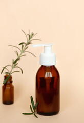 Brown glass bottle with a pump of cosmetic products framed by green leaf branches, beige background. Natural organic spa cosmetic beauty concept. Front view Mock up.