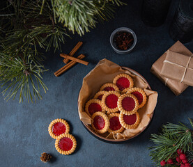 Homemade cookies with fruit  jam in a   bowl on a dark blue table with cinnamon, present box  and fir tree. Dark and mood image