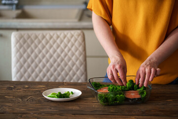 Close-up, a woman prepares a dish of red fish, salmon and broccoli in kitchen