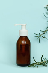 Brown glass bottle with a pump of cosmetic products framed by green leaf branches, blue background. Natural organic spa cosmetic beauty concept. Front view Mock up.