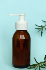 Brown glass bottle with a pump of cosmetic products framed by green leaf branches, blue background. Natural organic spa cosmetic beauty concept. Front view Mock up.
