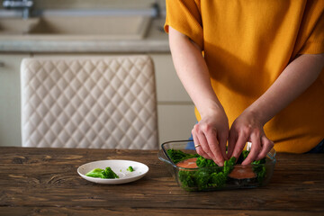 Close-up, a woman prepares a dish of red fish, salmon and broccoli in kitchen