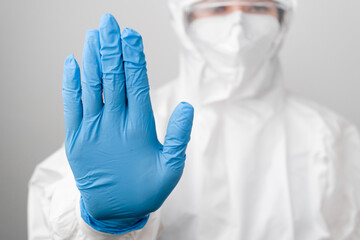 Doctor in a biohazard protective PPE suit and protective face mask against coronavirus, Sars-Cov-2, Covid-19 shows sign stop in blue rubber gloves.
