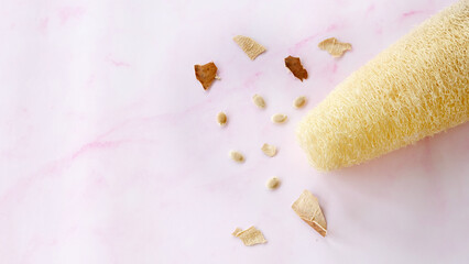 Dry and clean loofah with some luffa fruit skin pieces scattered around, on a pink marble background.