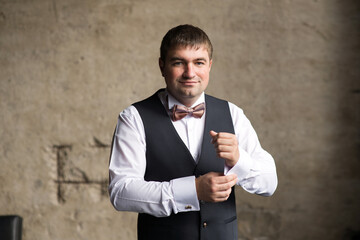 A man in a vest fastens a cufflink on his sleeve