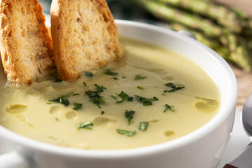 Fresh green asparagus soup in bowl on rustic wooden table. Close up