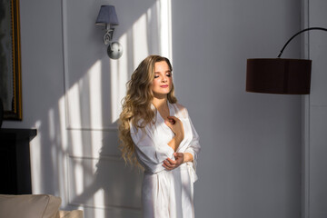 Fototapeta na wymiar Beautiful bride in a peignoir under the rays of the sun in a hotel room