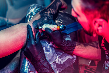 Tattoo artist in black gloves making a tattoo on the arm of man