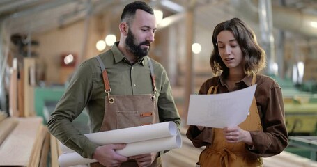 Video portrait of a two enthusiastic carpentry workers, designing some wood products at the workshop. Standing together with drawings smiling in the joinery