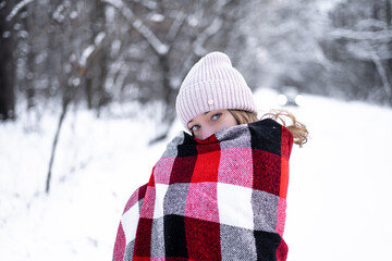 girl with blue eyes in a snowy forest is wrapped in a red checkered scarf looks mysteriously