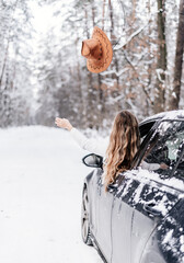 the girl gets out of the car and throws her hat in the winter forest