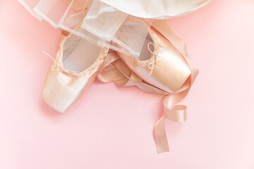 New pastel beige ballet shoes with satin ribbon and tutut skirt isolated on pink background. Ballerina classical pointe shoes for dance training. Ballet school concept. Top view flat lay, copy space
