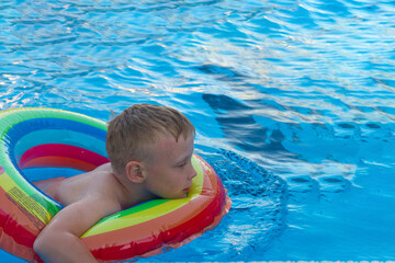 Fototapeta na wymiar A boy swims on an inflatable colorful circle in a pool with blue clear water in the summer.