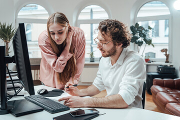 Bearded boss with glasses and curly hairs does his paperwork with his attractive secretary in comfortable office room.